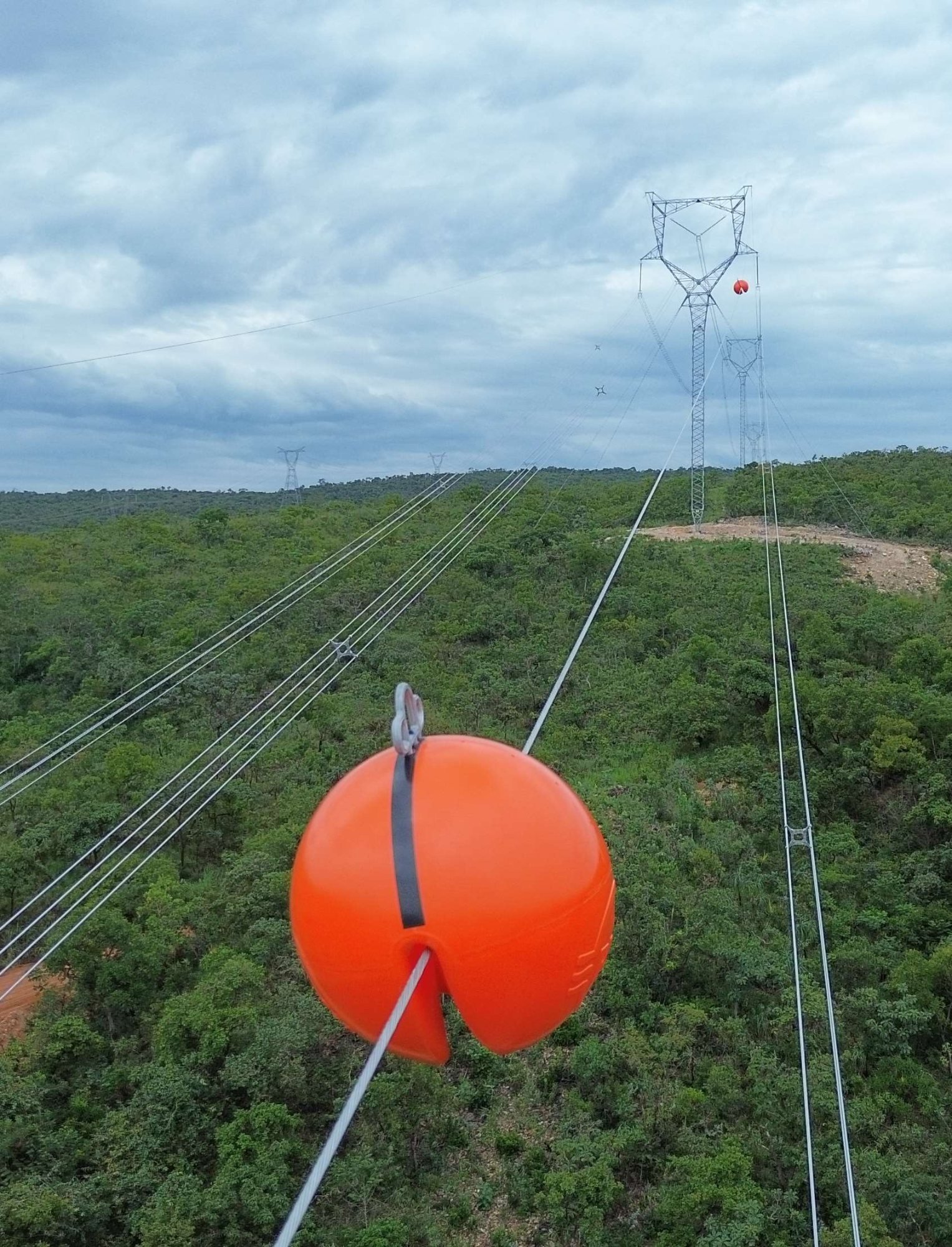 Esfera de sinalização aérea laranja instalada em cabo de Linha de Transmissão, drone visível ao fundo contra céu nublado