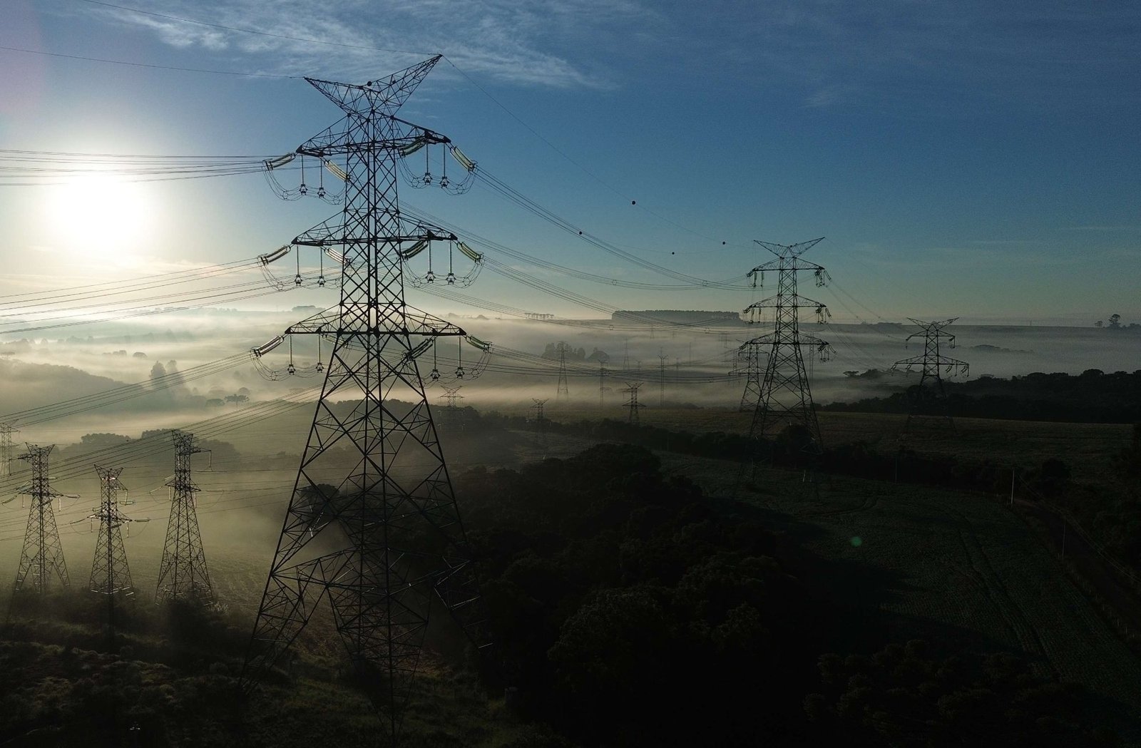 Torres de Linha de Transmissão na neblina ao amanhecer, vistas de baixo contra o sol nascente