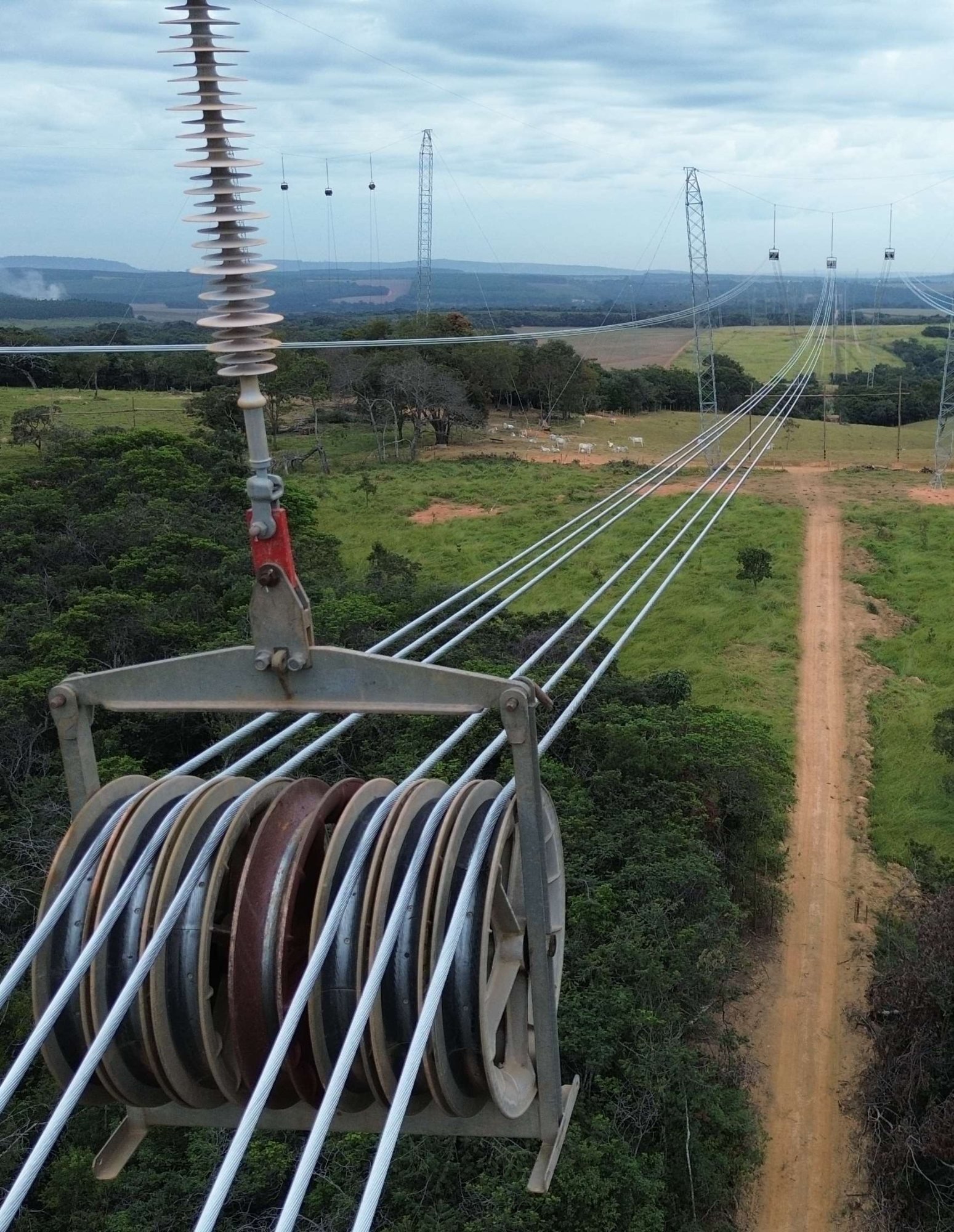 Carretéis de cabo condutor e isolador de Linha de Transmissão, com torres ao fundo sob céu nublado